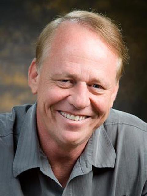 Thomas J Meade smiling to camera in grey shirt