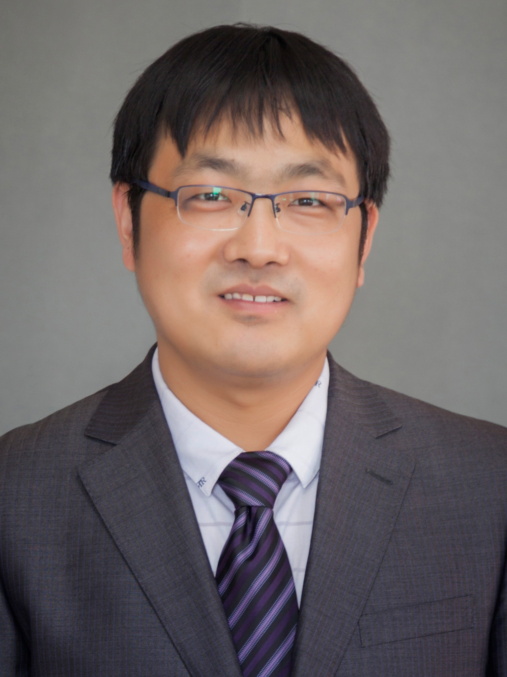Xianfeng Li smiling to camera wearing glasses and suit and tie