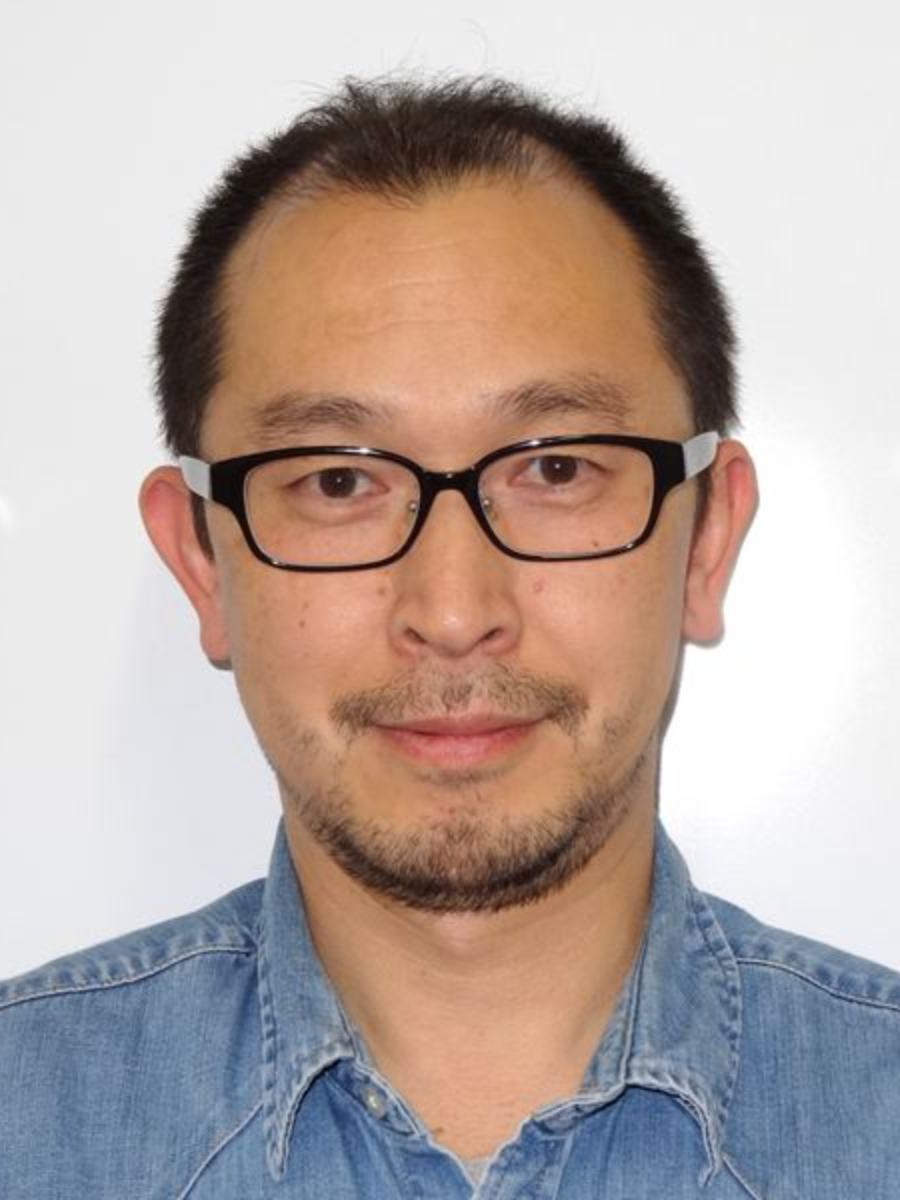 Toshiharu Teranishi smiling to camera with a faint beard and wearing glasses