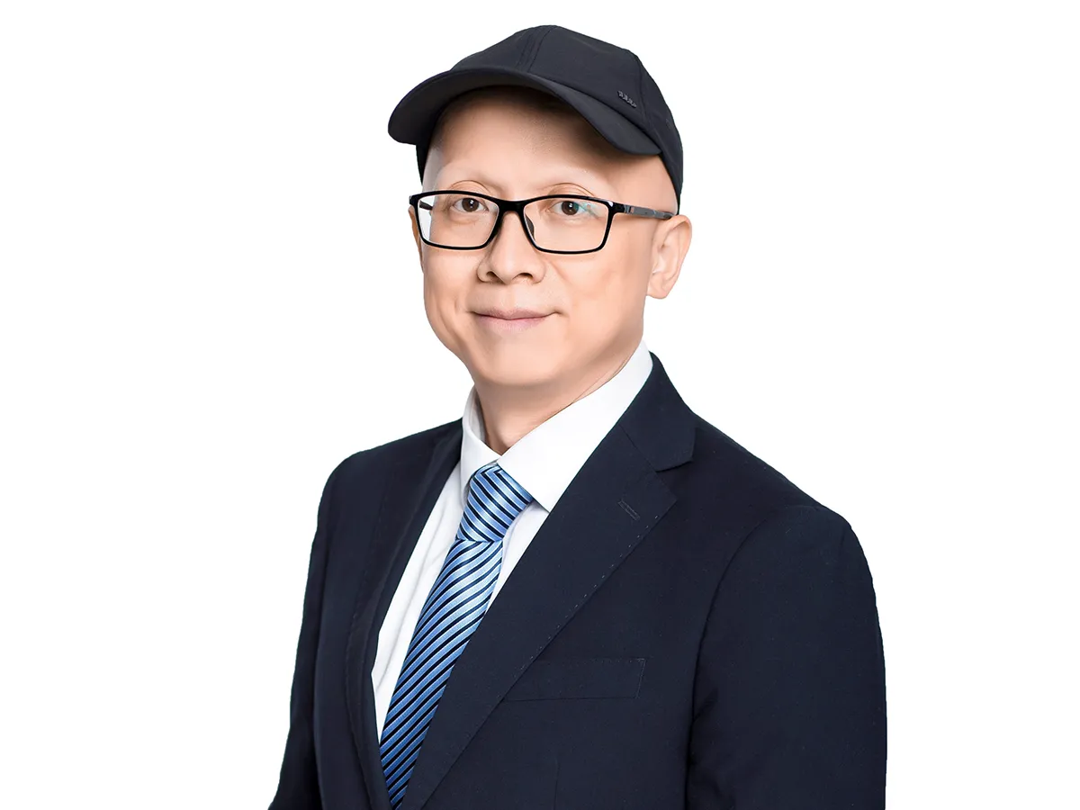 Professor Xingyu Jiang professional headshot in a suit and baseball cap and glasses