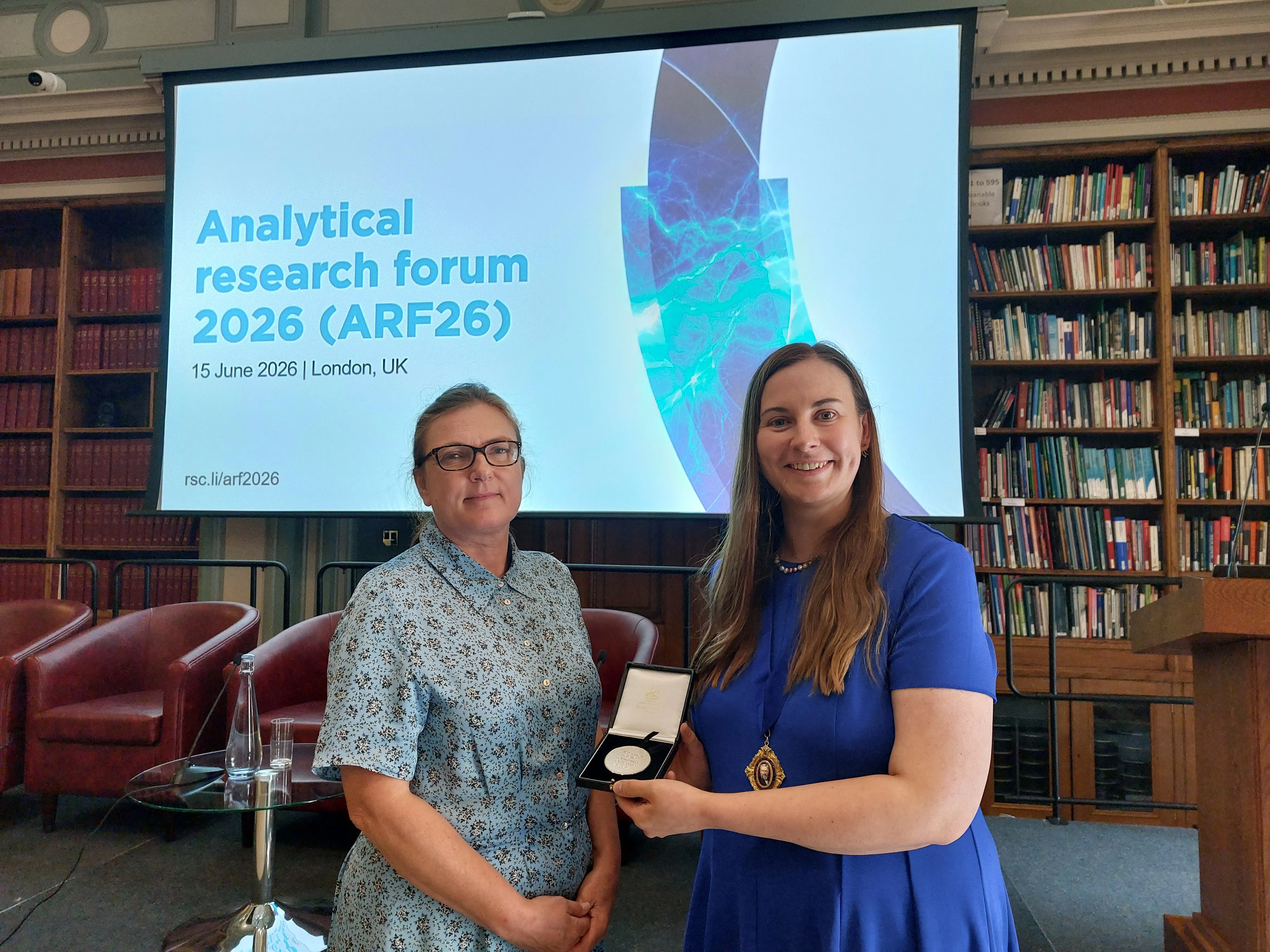 Zoe Ayres receives a medal to honour her time as Chair of the Analytical Board a woman holding a medal and standing next to another woman