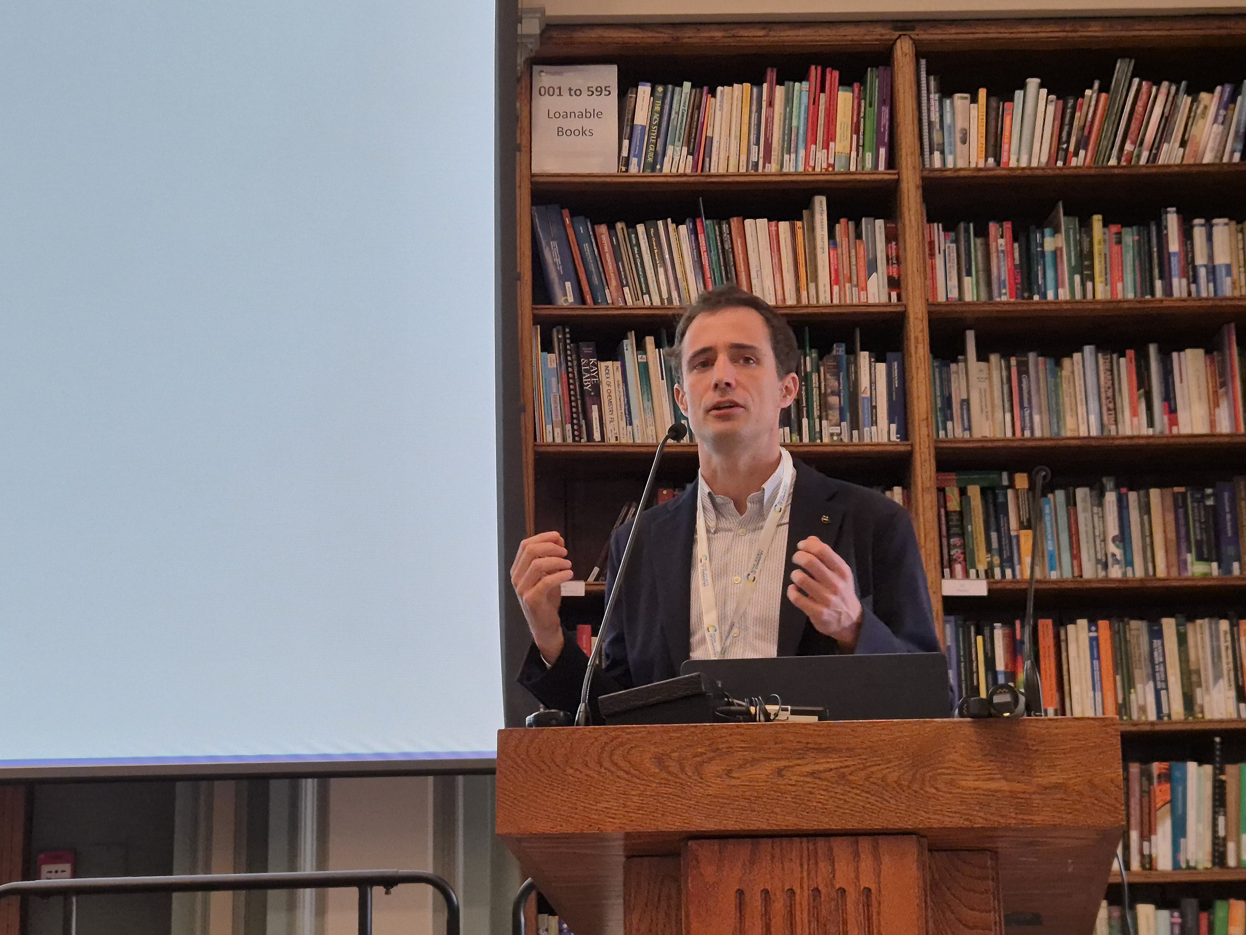 Dr Pietro Sormanni standing at a podium with a microphone in front of a bookcase