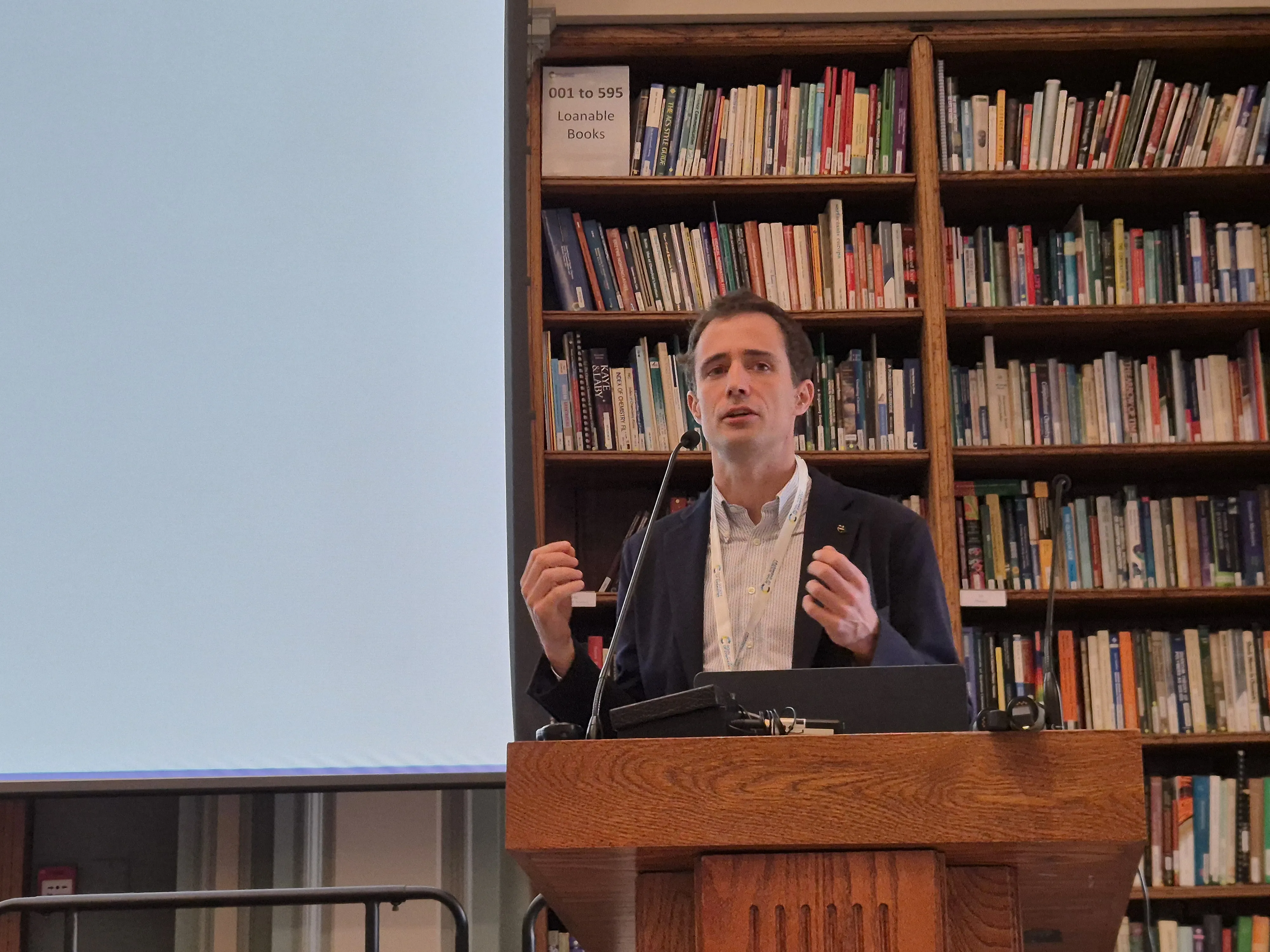2026 Chemical Biology Symposium - Dr Pietro Sormanni gives a presentation Dr Pietro Sormanni standing at a podium with a microphone in front of a bookcase