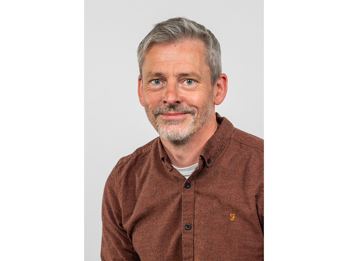 Professor Dave Adams headshot, smiling and wearing brown shirt