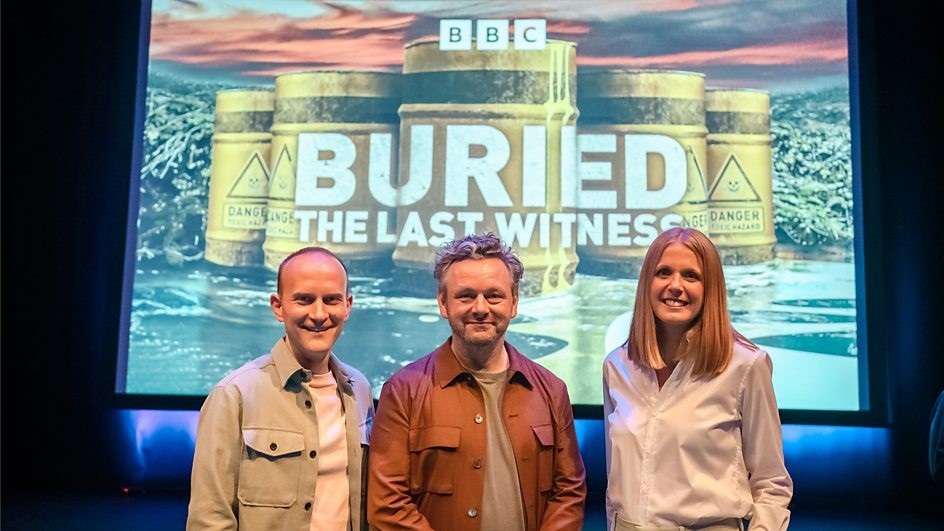 Actor and campaigner Michael Sheen (centre) with investigative reporters Dan Ashby and Lucy Taylor stand in front of a screen that has the logo for the 'Buried: The Last Witness' series