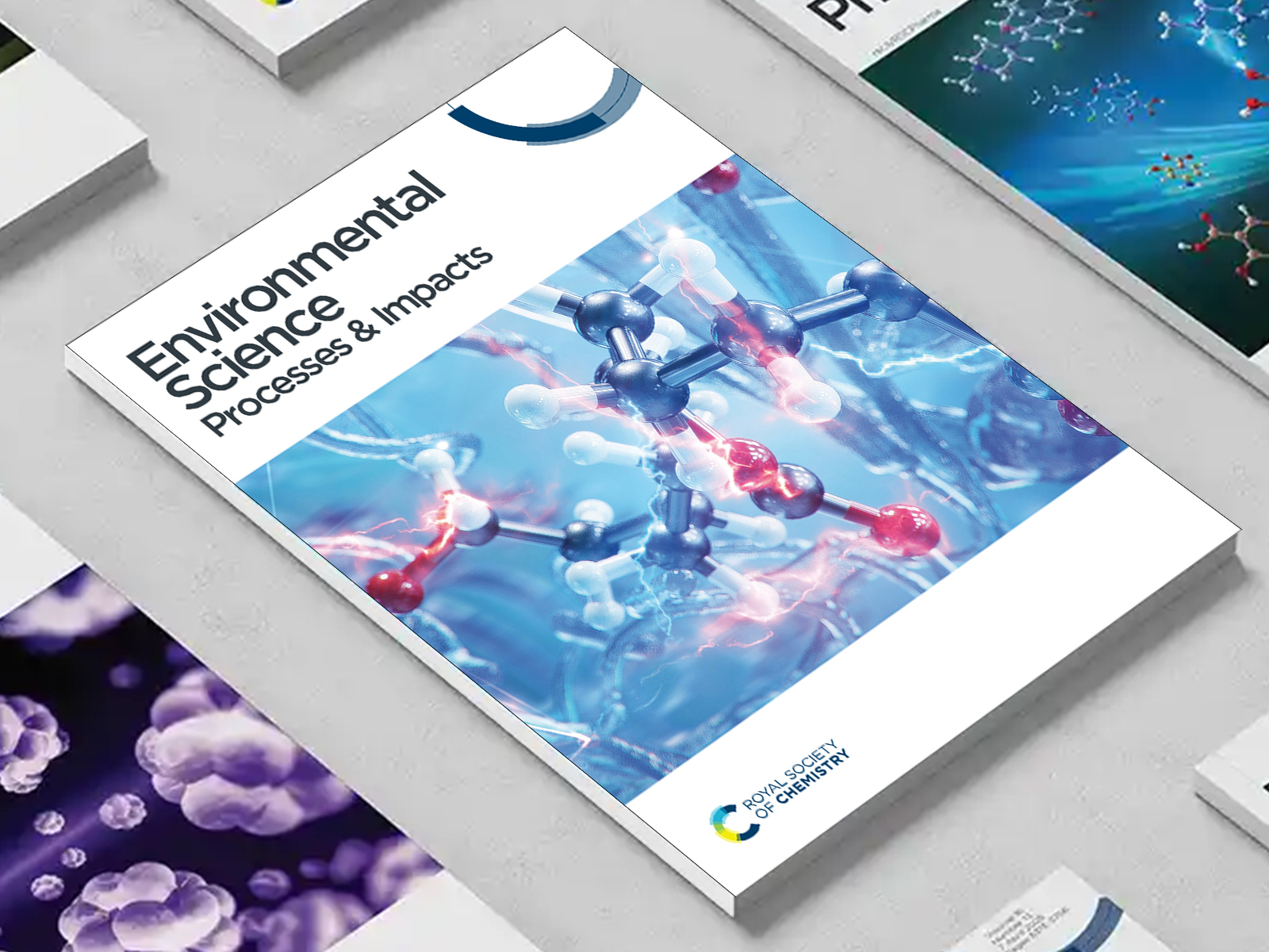 the Environmental Science Processes & Impacts journal among a group of other journals on a desk
