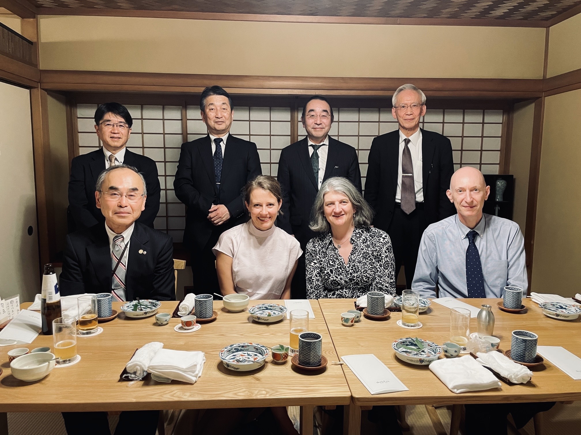 Two rows of four people sit and stand around a dinner table in Tokyo, Japan. The RSC's Sara Bosshart, Helen Pain and Anthony Galea sit second left, second right and right in the front row.