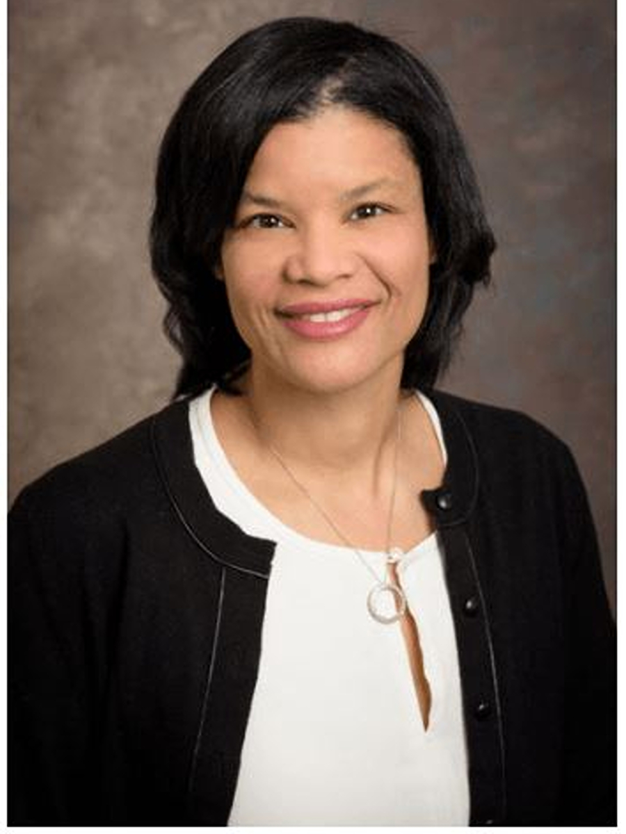 Headshot of LaShanda Korley, smiling gently at the camera. She is wearing a black cardigan with neutral grey background.