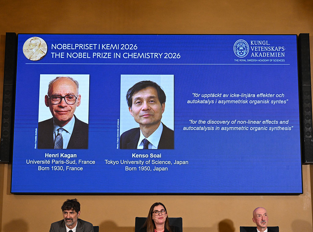 (Bottom L-R) Heiner Linke, Ellen Moons and Peter Somfai react in front of a screen displaying this year's laureates Henri Kagan and Kenso Soai.