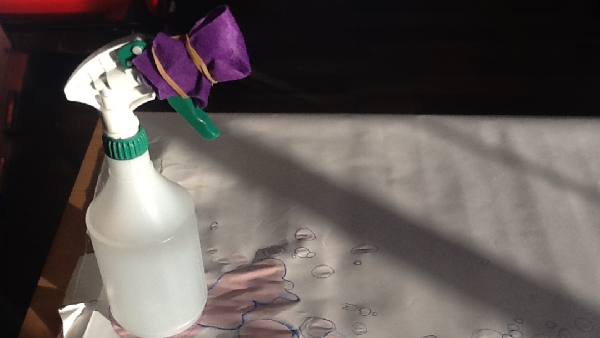 A spray bottle being used for a textile design process, possibly involving tie-dye or fabric painting