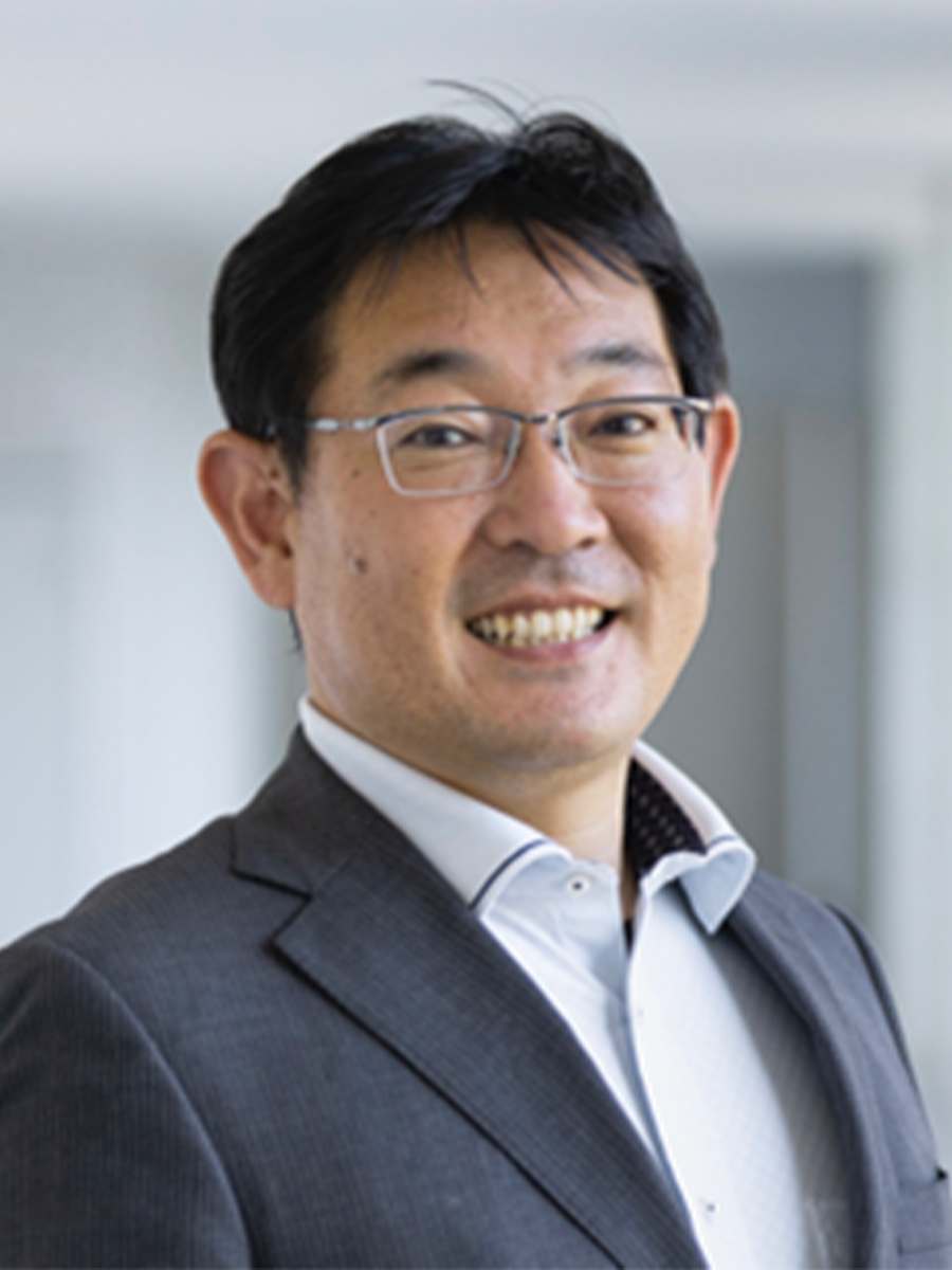 Atsushi Wakamiya smilng at the camera, wearing glasses and suit