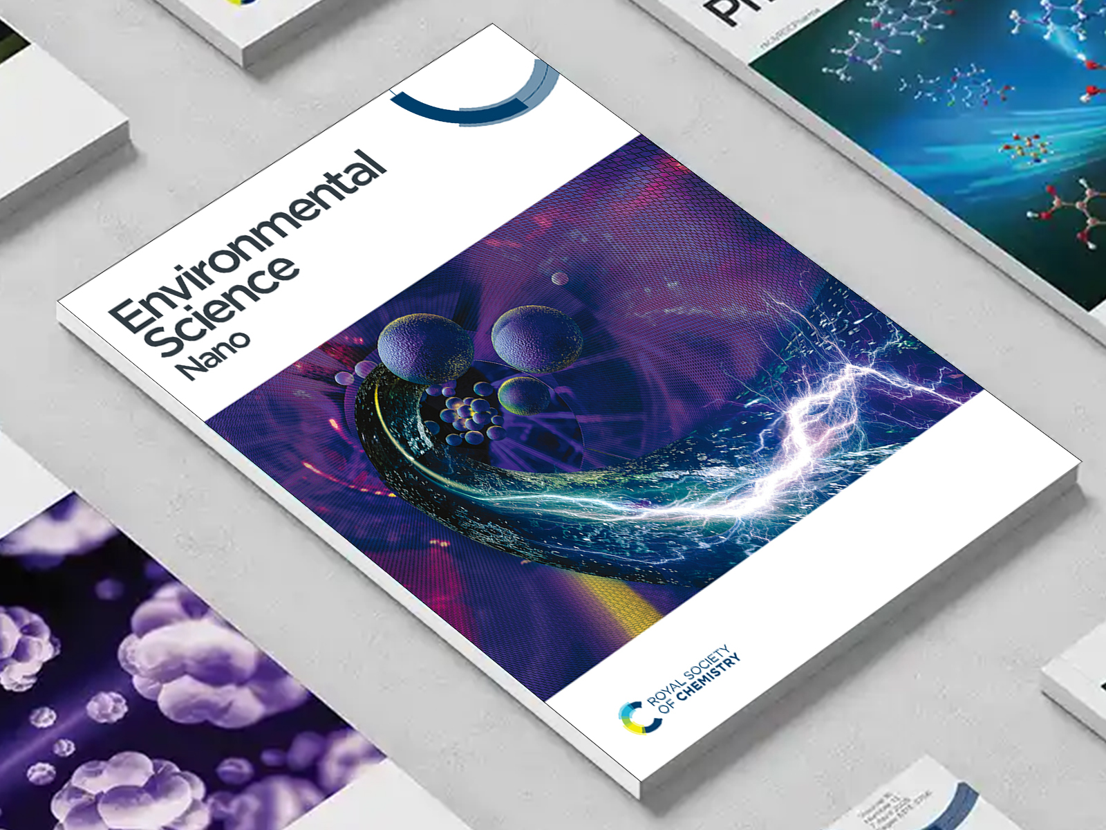 the Environmental Science Nano journal among a group of other journals on a desk