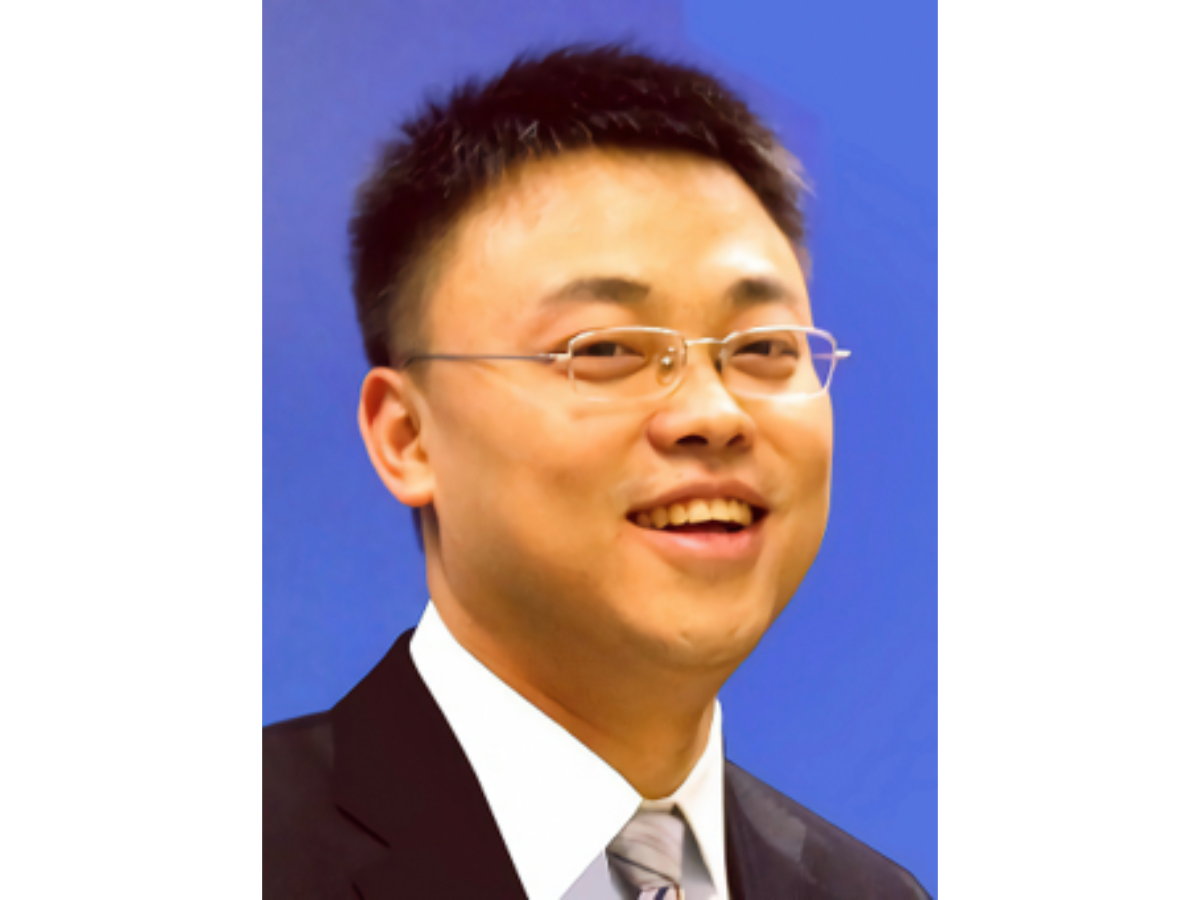 Xu Hou in a suit and tie and glasses smiling to camera