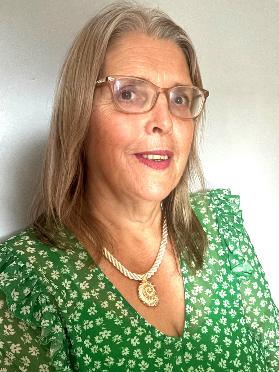 Joanne Davies smiling to camera in green floral dress and glasses