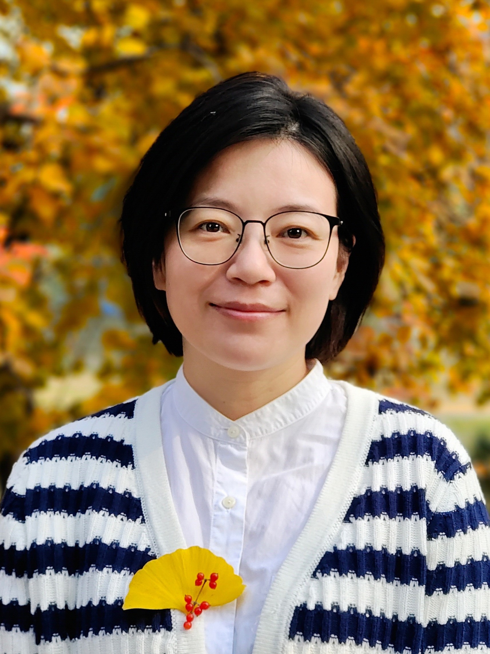 Wenjun Liu, smiling at the camera wearing eyeglasses and dark blue stripey cardigan.