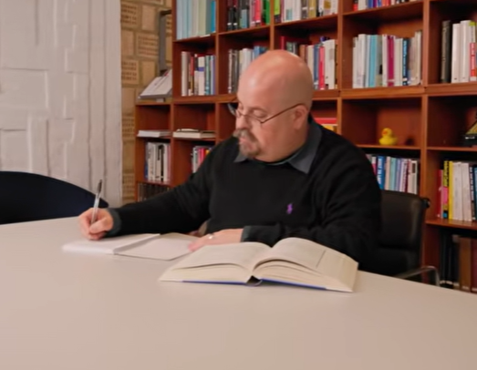 a man sitting at a table writing on a book