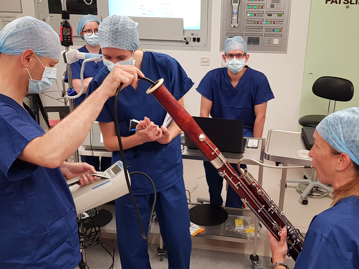 The PERFORM COVID-19 Team wearing scrubs and surgical caps, experimenting in the lab with a saxophone