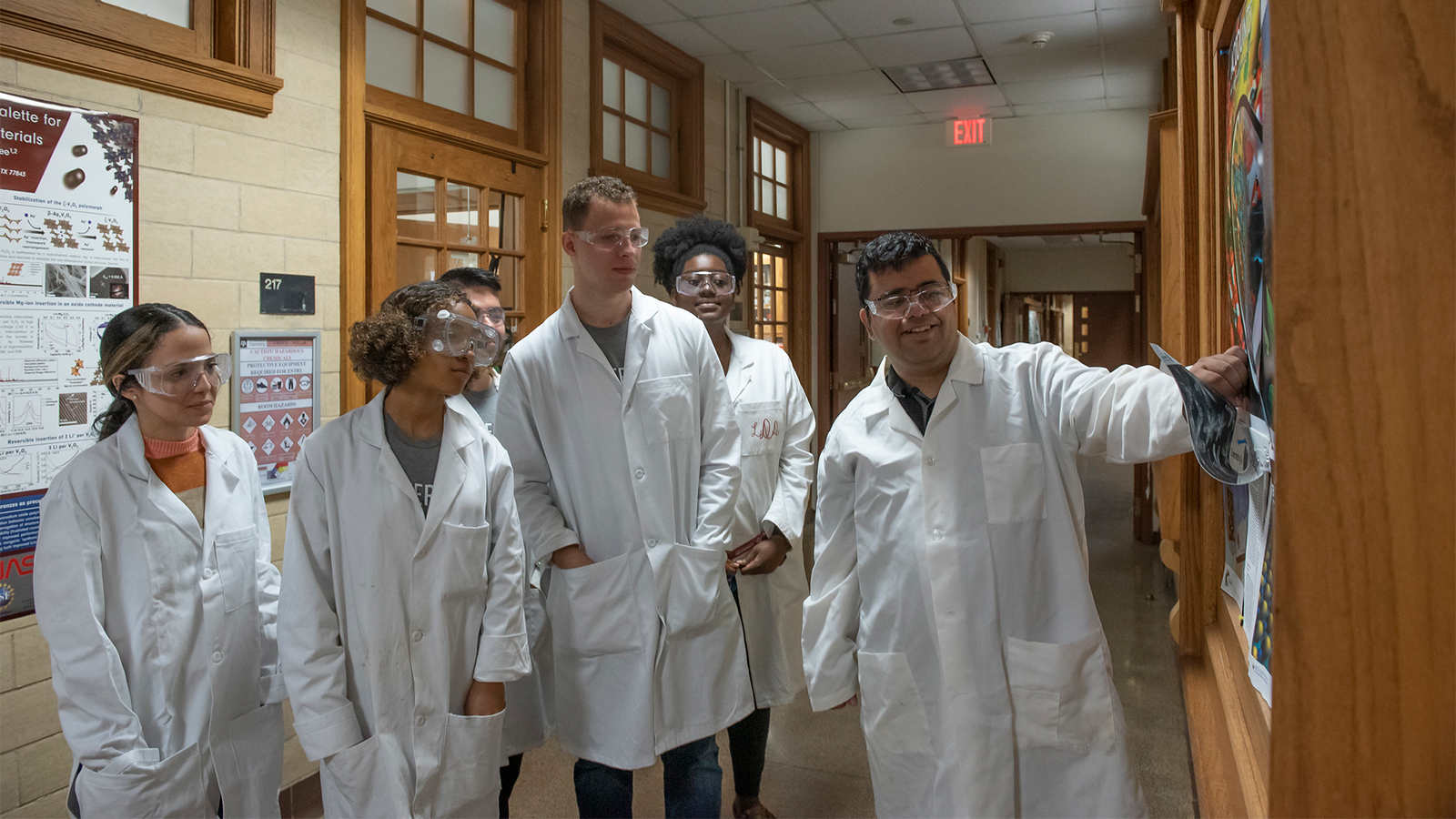Professor Sarbajit Banerjee demonstrating with group of scientists wearing white lab coats and goggles