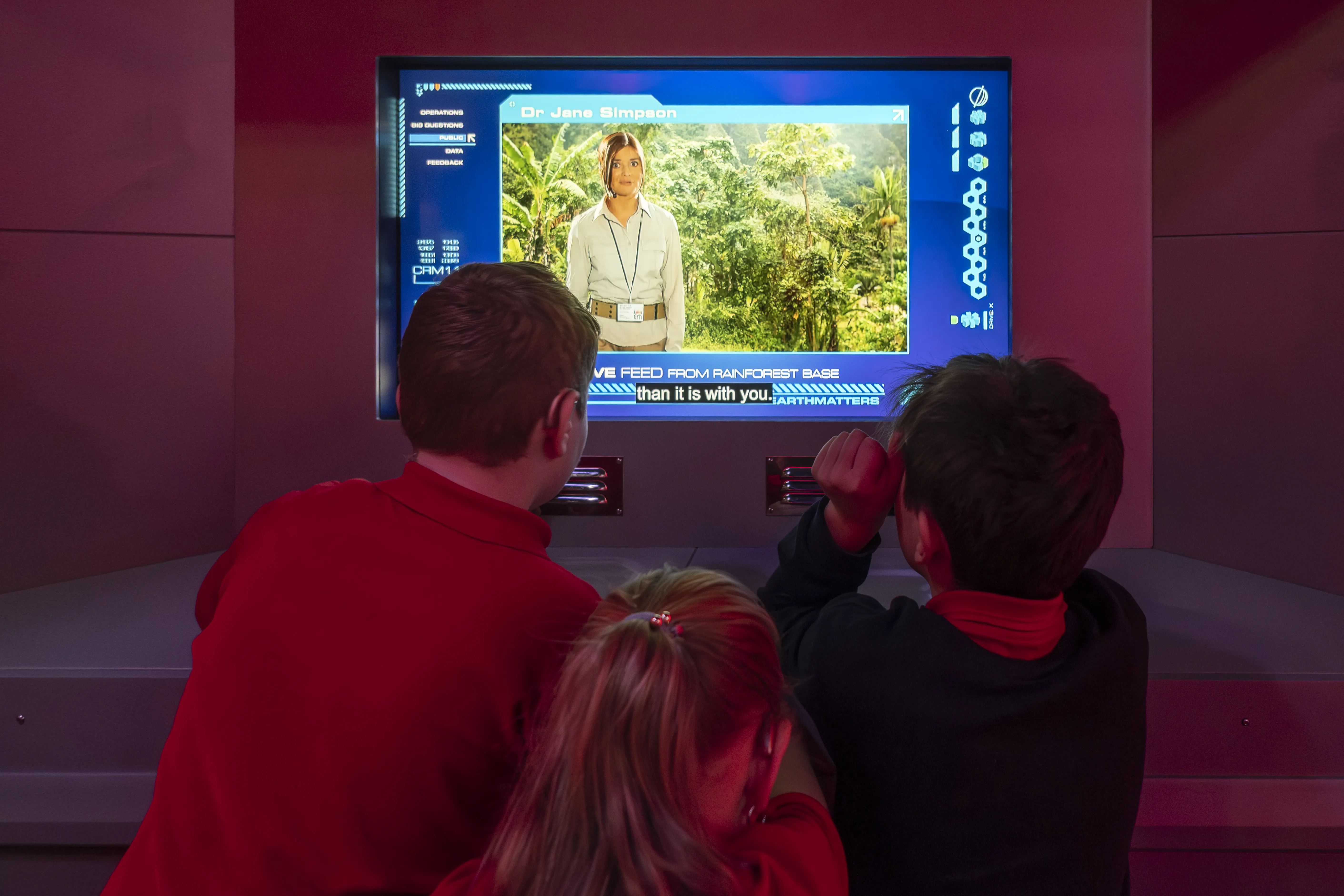 Deaf Science day_learners explore exhibit - credit Robin Mair Photography a group of people are enraptured by a monitor showing the rainforest