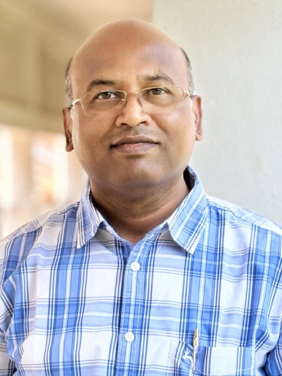 Nagula Shankaraiah headshot, wearing blue and white checked shirt and glasses