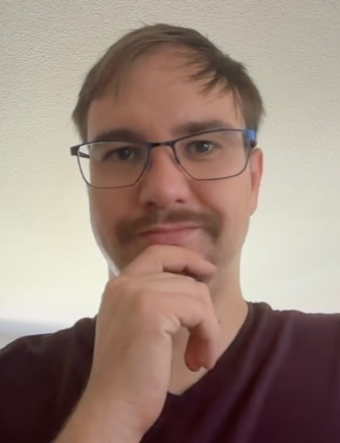 Alexander Hopp with light brown hair, glasses, and a mustache posing thoughtfully with his hand on his chin.