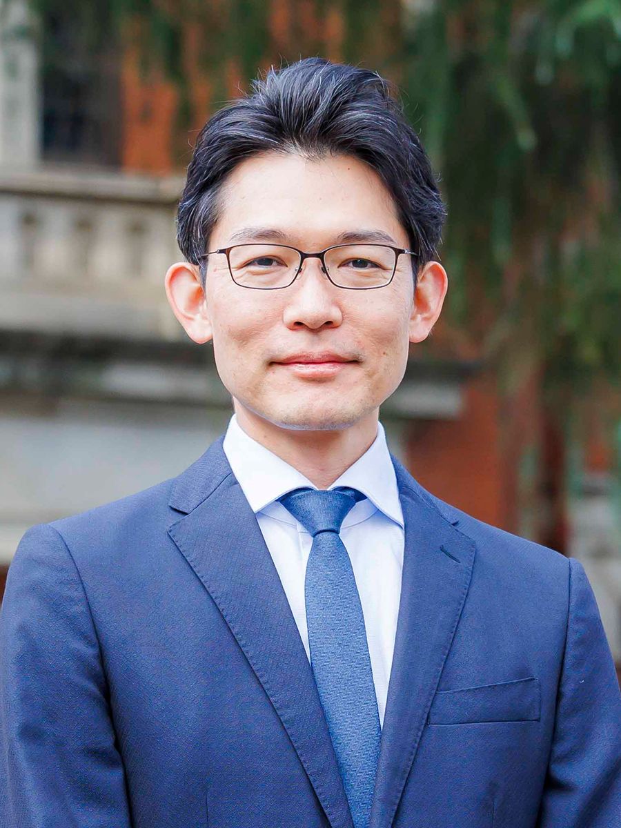 Nobuhiro Yanai in blue suit and tie, wearing glasses and smiling to camera