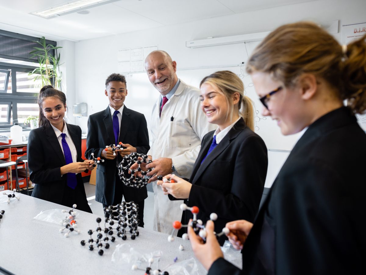 School children in uniform in classroom with teacher creating ball and stick models