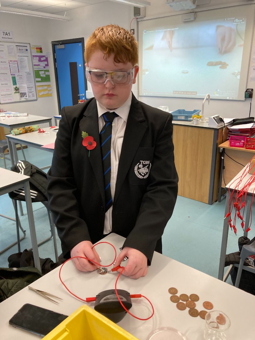 A boy wearing safety goggles conducts a battery experiment