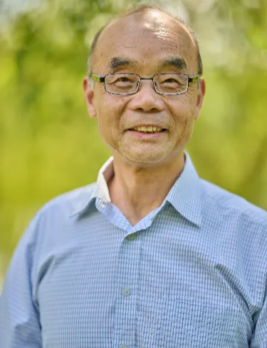 Huafu Wang Huafu Wang smiling, wearing glasses and a light blue patterned button-up shirt, set against a softly blurred green background.