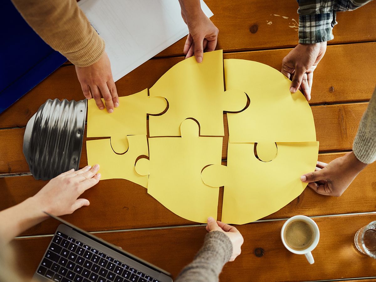a group of people assembling an oversize puzzle that creates a lightbulb