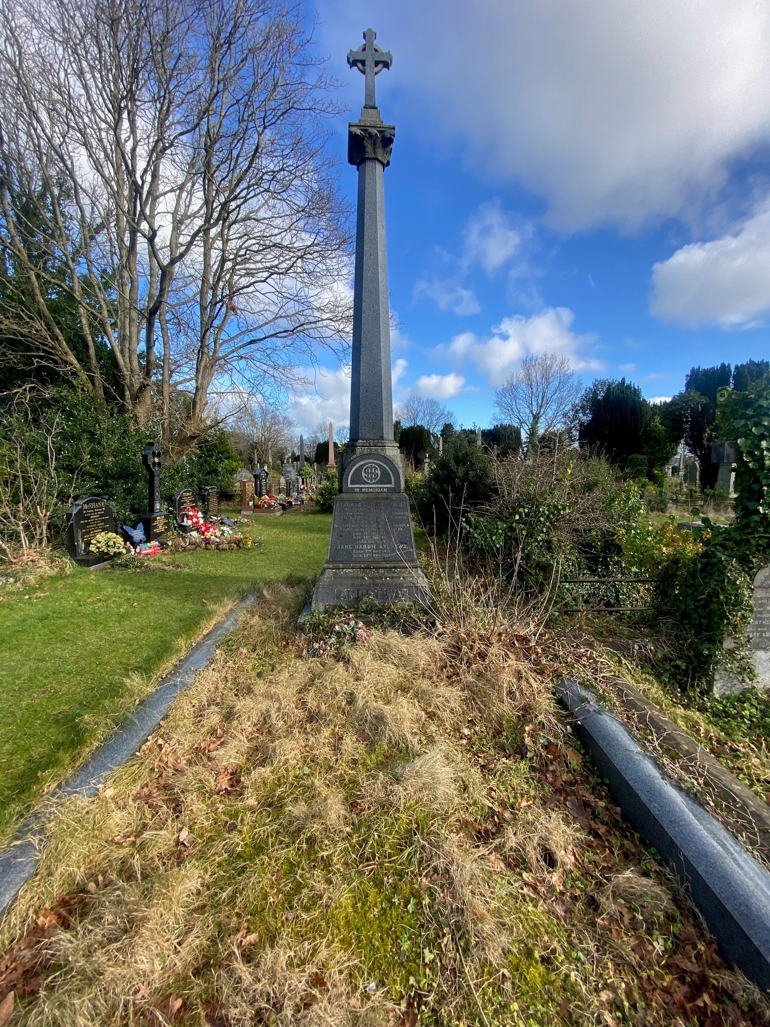 The grave was in an overgrown state before the restoration, with long grass and weeds surrounding the unkempt base