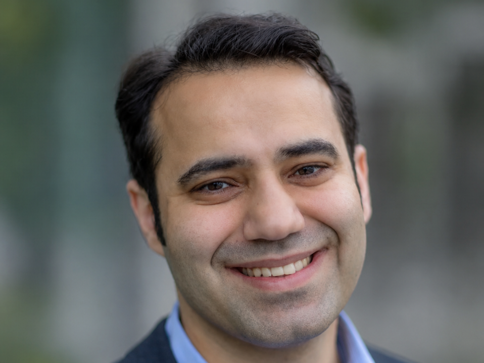 Headshot of Michael Saliba smiling, wearing a blue collared shirt under a dark jacket.