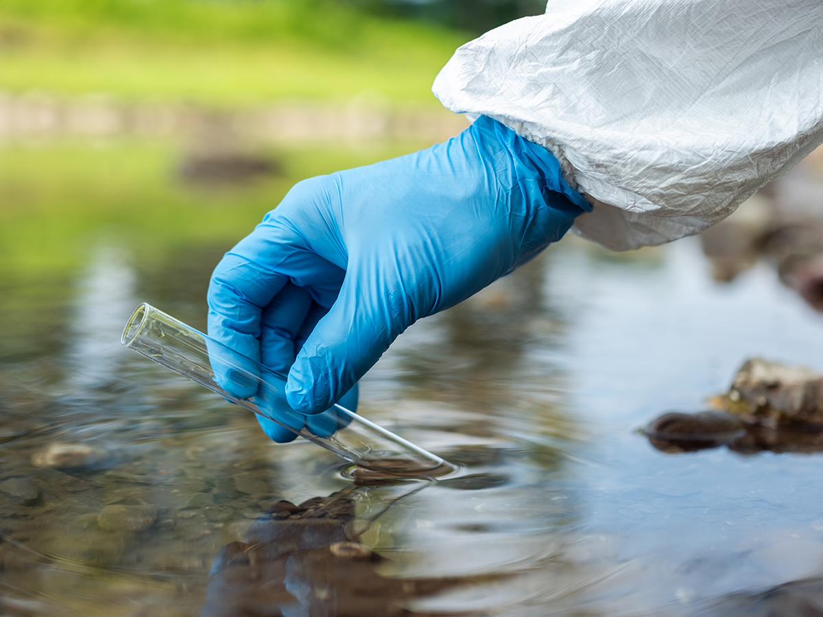 Hand wearing glove sampling water using test tube