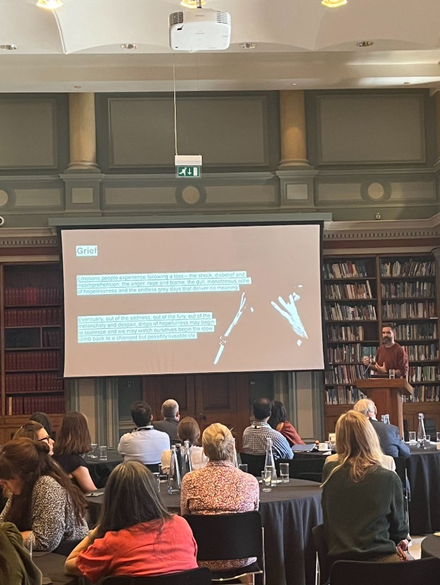 Dr Stephen Hughes standing and presenting to a crowd inside Burlington House