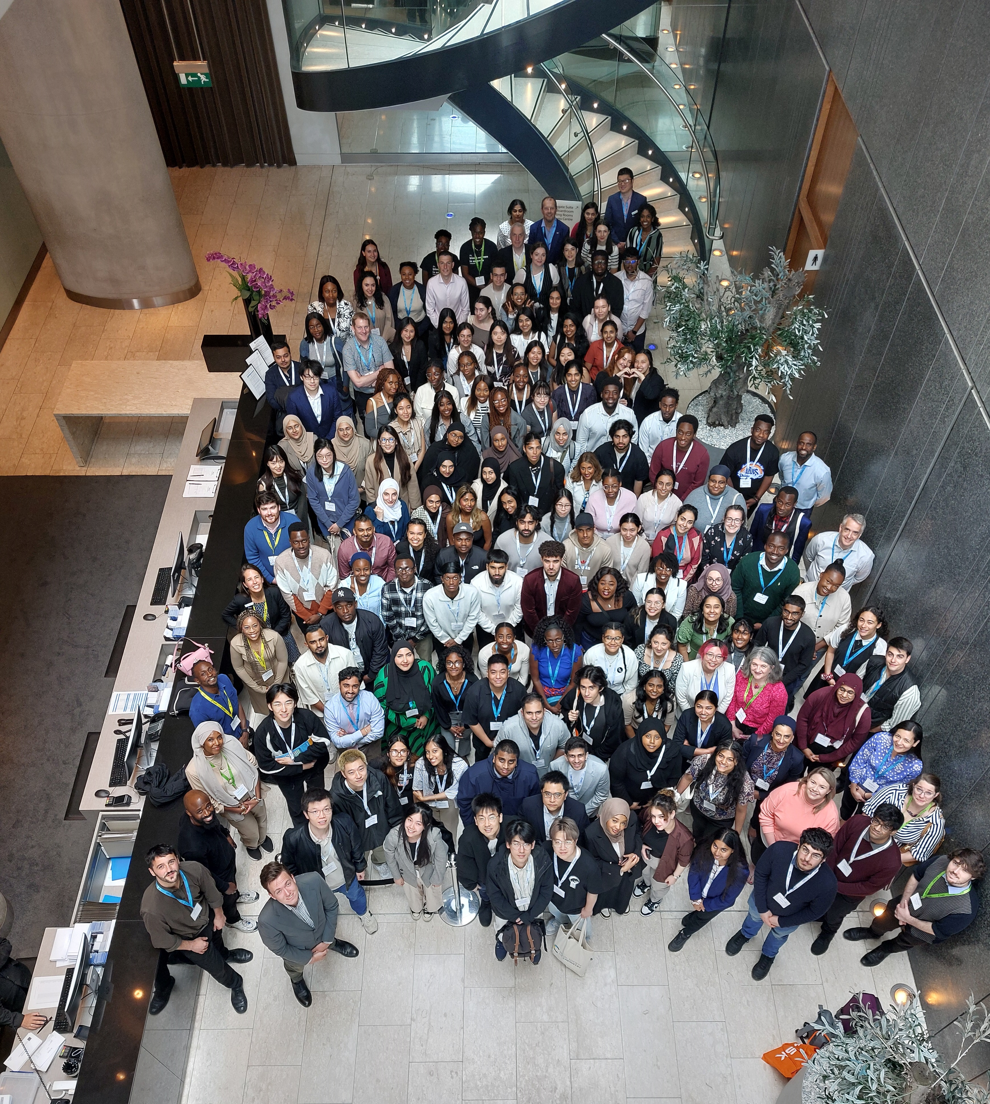 More than 100 young Black and minoritised ethnic chemical scientists, company representatives and RSC staff stand in the reception area of a hotel while looking up towards the camera and smiling
