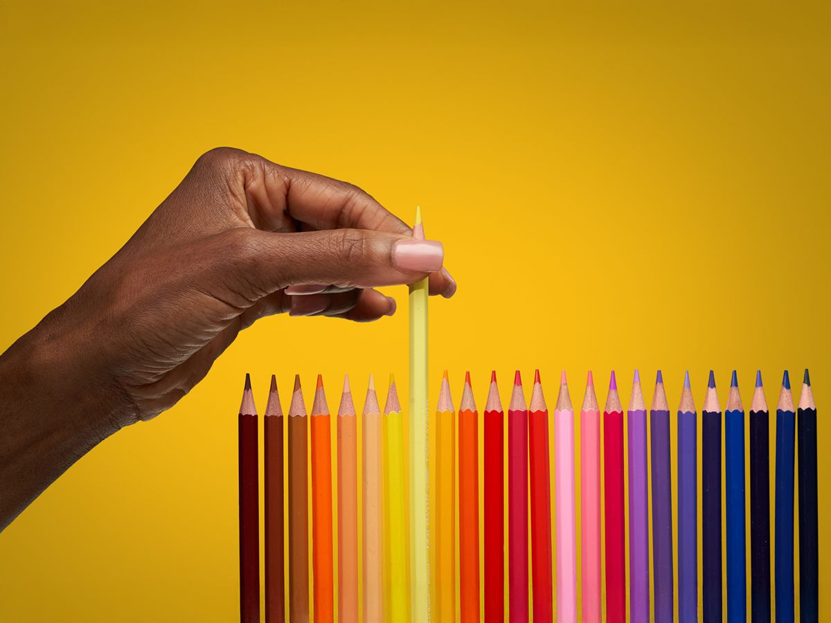 a hand with black skin tone choosing a pencil from a row of rainbow coloured ones