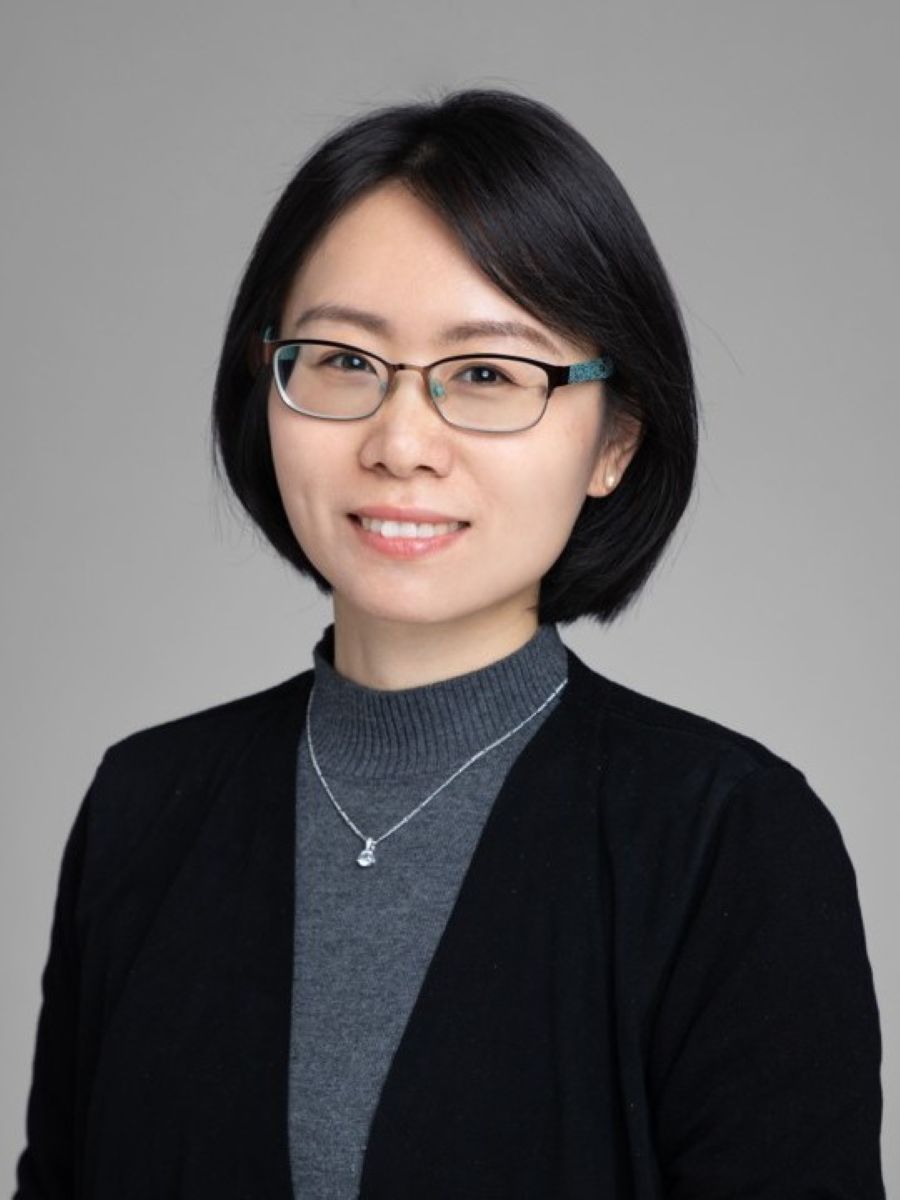 Huilin Pan smiling to camera wearing glasses, silver necklace, grey jumper and black suit jacket