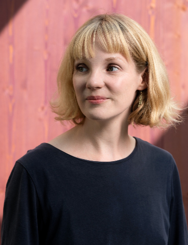 Linn Leppert with blonde bob haircut with bangs, wearing a dark, long-sleeved shirt and looking slightly to her right.