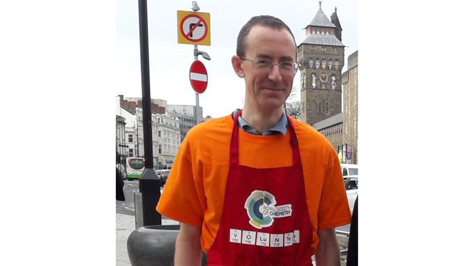 Dr James Redman standing outside as if being interviewed, wearing an orange shirt and red apron with our RSC logo