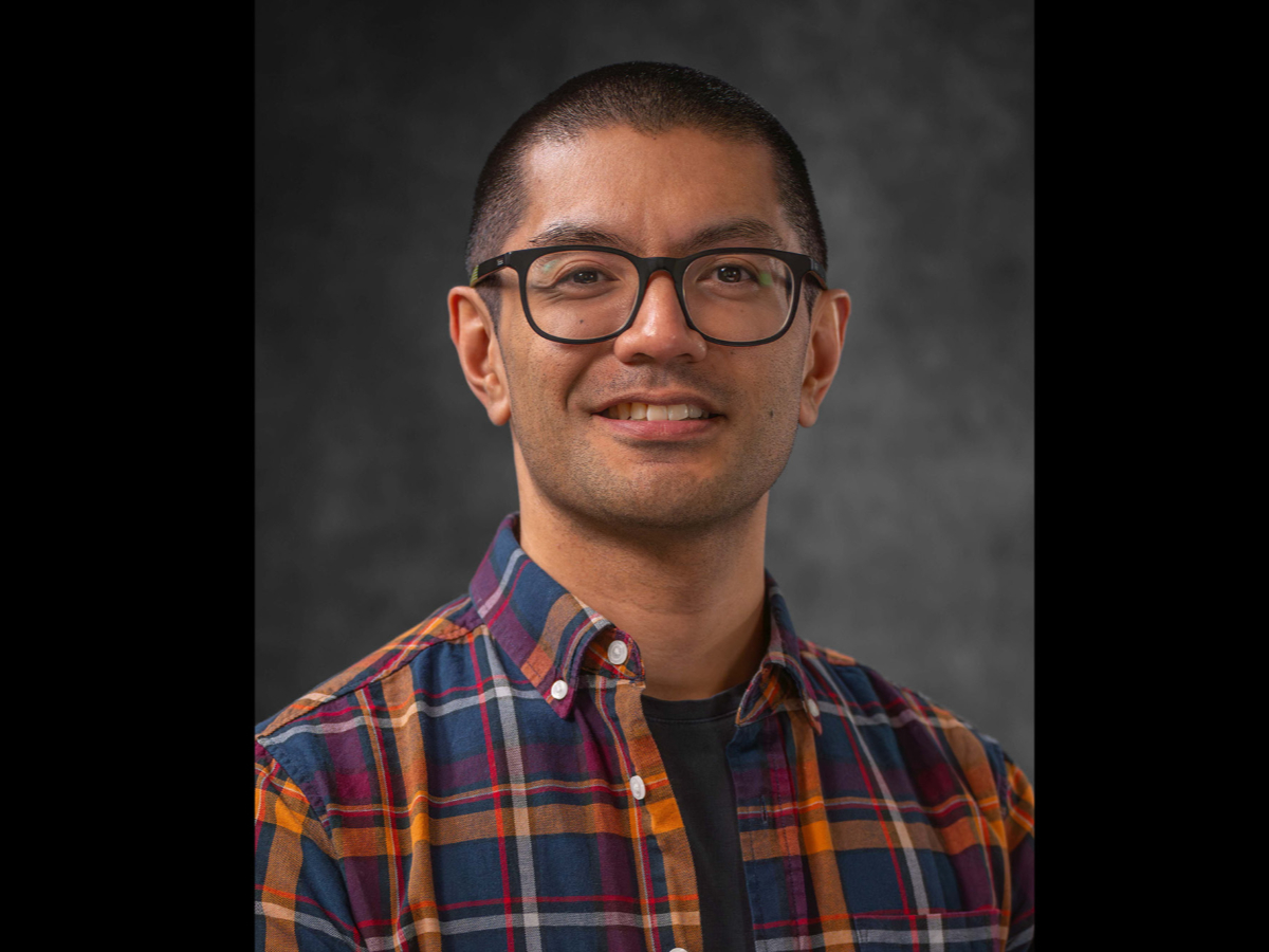 Benjamin Arenas smiling to camera in check shirt and glasses