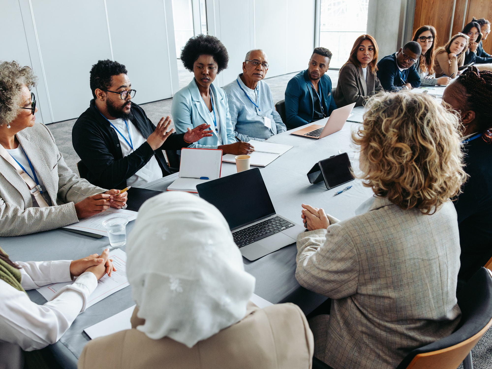 A group of mixed race and gender people discuss around a table with laptops