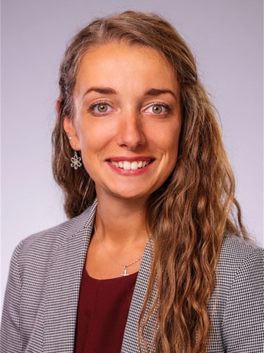 Michele Sarazen with long hair wearing a suit jacket smiling to camera