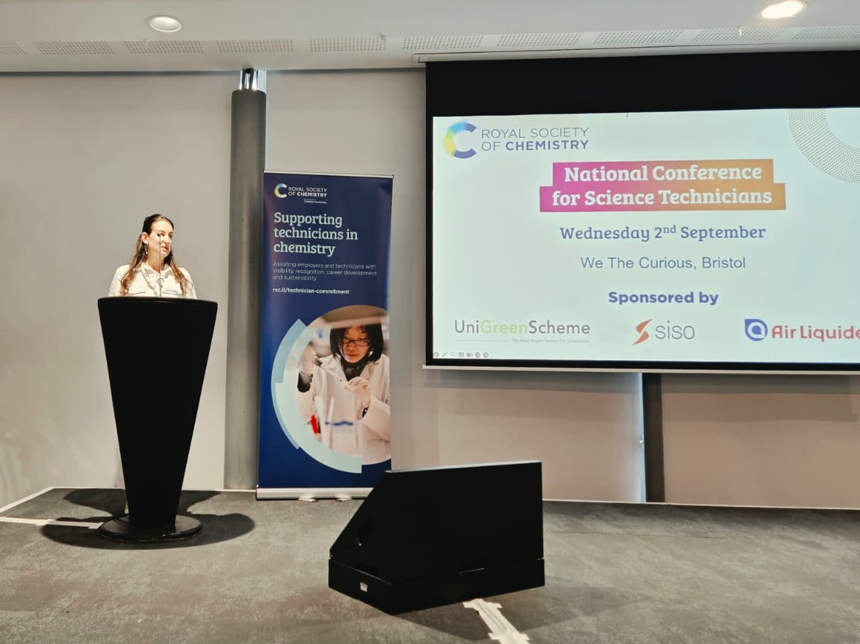 Catherine Perry, of the Royal Society of Chemistry, standing at a podium with a screen displaying the words "National Conference for Science Technicians"