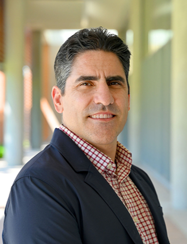 Rafael Verduzco smiling at the camera, wearing a chequered shirt under a dark blue blazer