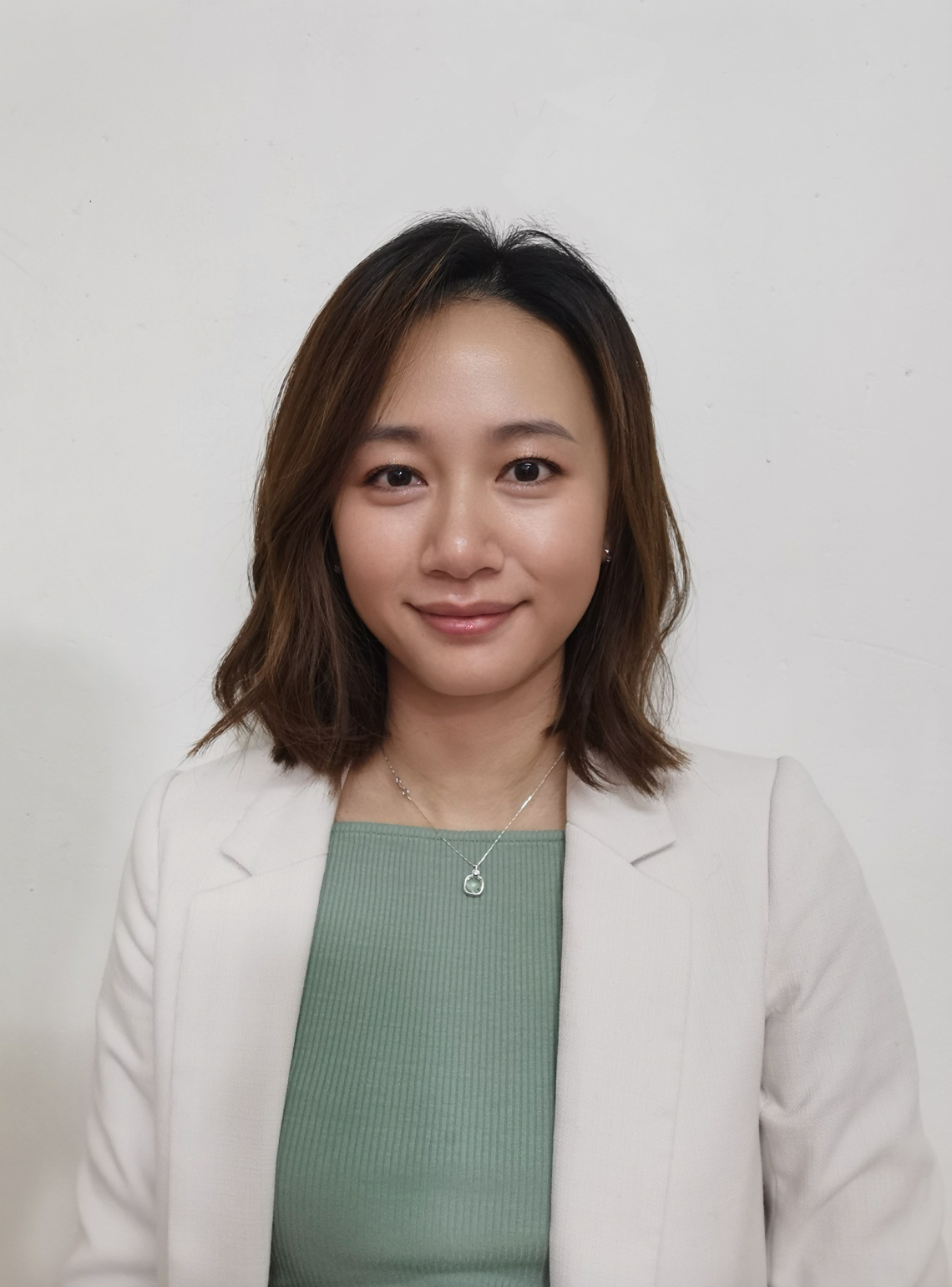 Iris Yu smiling against a plain, light background. She is wearing a light green top underneath a white blazer.