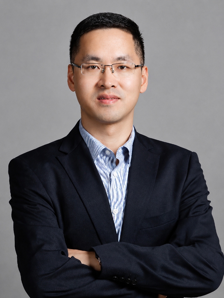Qiang Liu smiling, wearing a dark blazer with his arms crossed against a solid grey background.