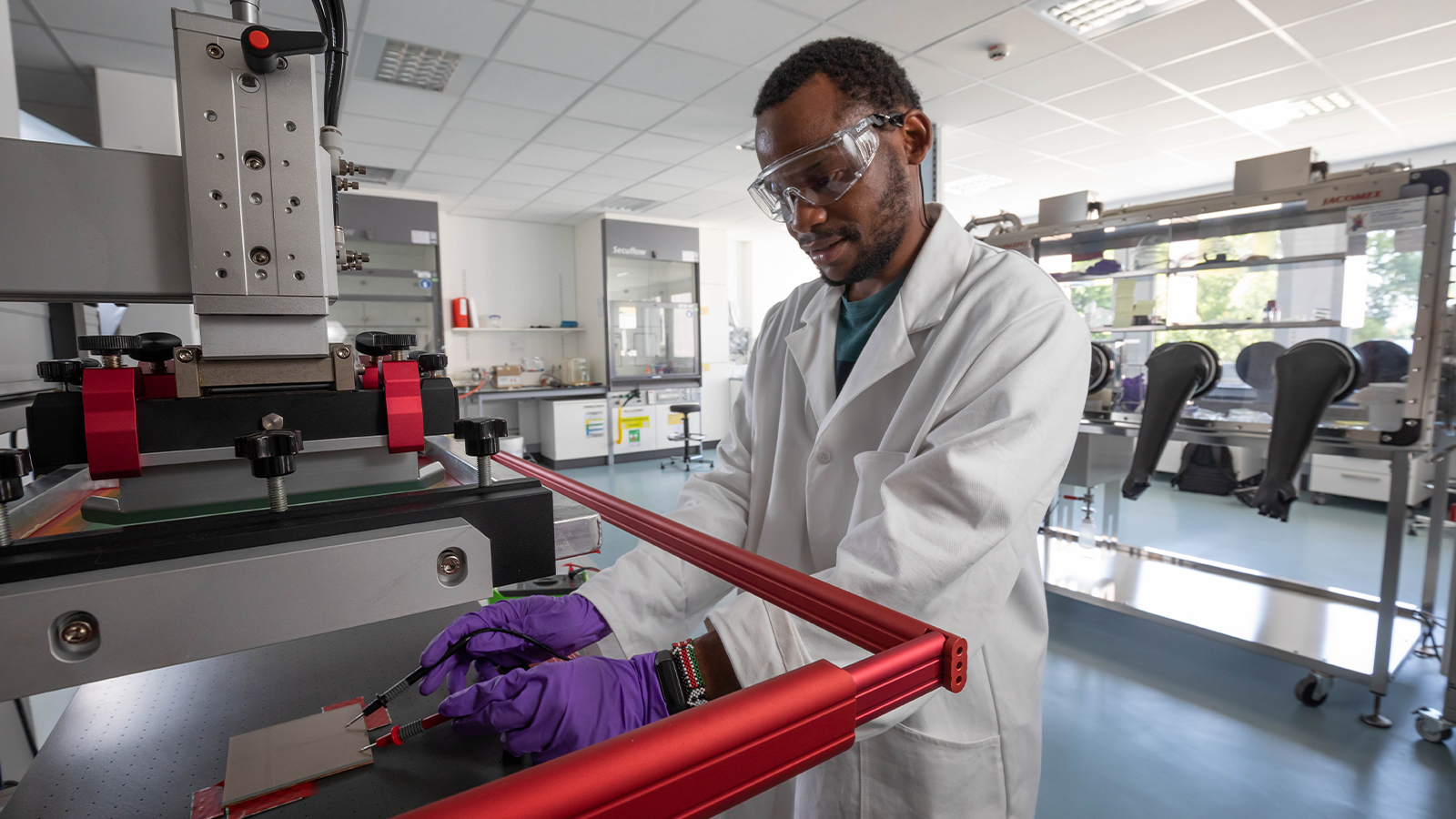 PISCO Team member wearing goggles and white coat working at machinery in a lab