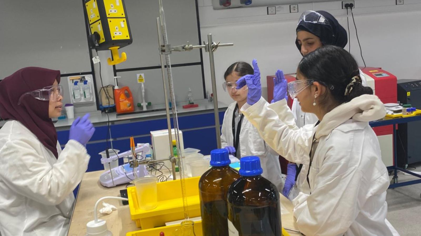 Syrian refugee school children at chemistry workshop, wearing lab coats and blue latex gloves, safety glasses