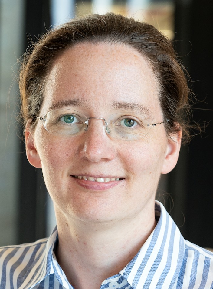 Laura Herz smiling gently at the camera and wearing a light blue and white vertical-striped button-down shirt.