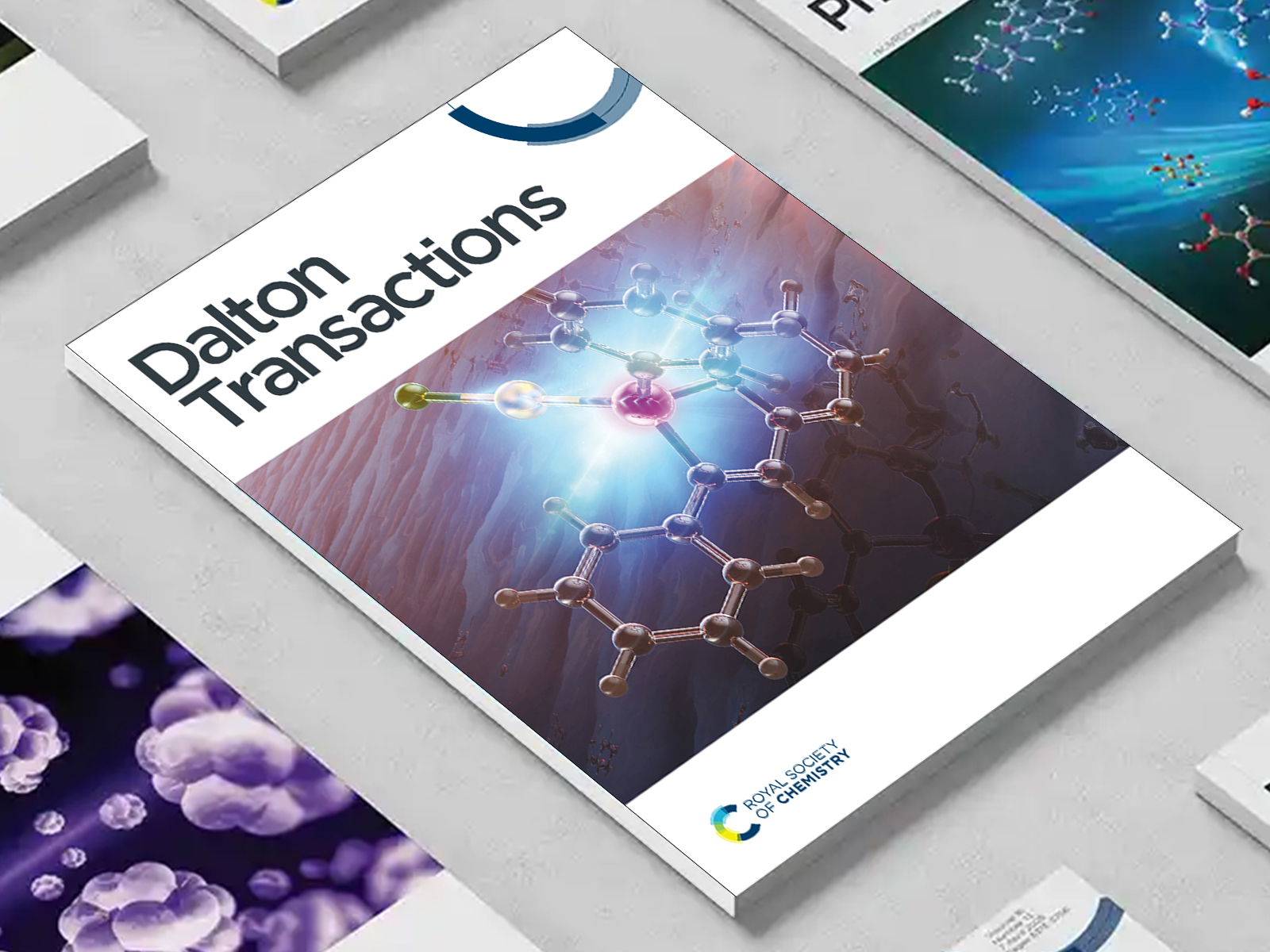 the Dalton Transactions journal among a group of other journals on a desk